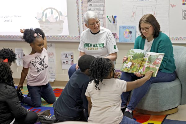 Two instructors read aloud to elementary students in a classroom from an open book.