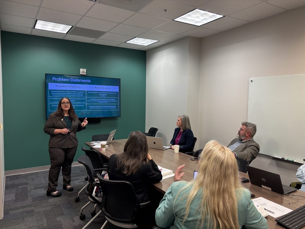 Merry defends her dissertation to a committee of five faculty in a conference room.