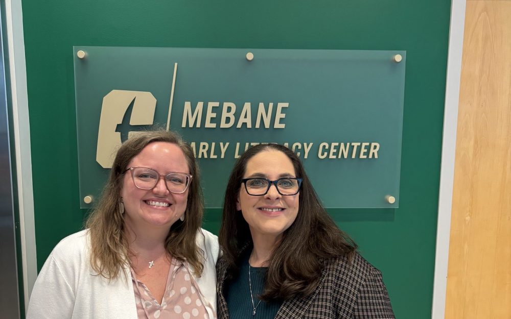 Director Angela Preston and admin support Jennifer Merry pose in front of the Mebane Early Literacy Center sign