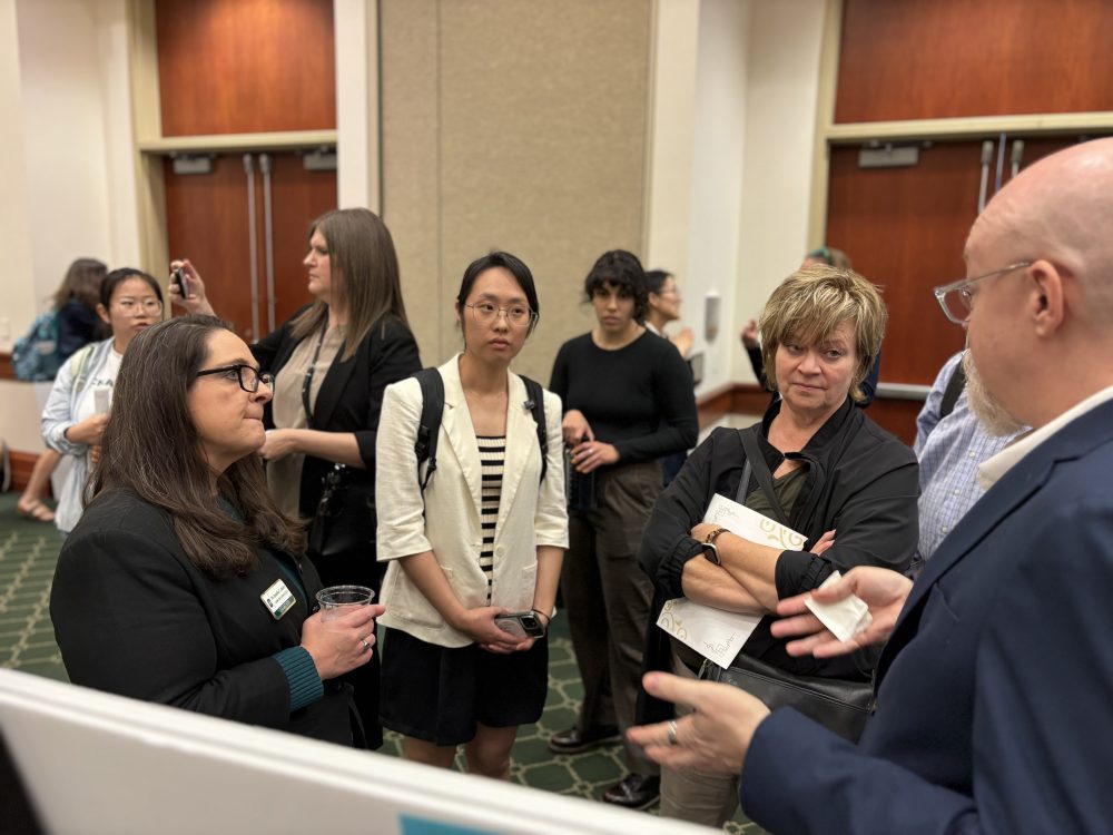 Merry presents a research poster with fellow Ph.D. student Rudy Hawley to a small crowd in a convention center room